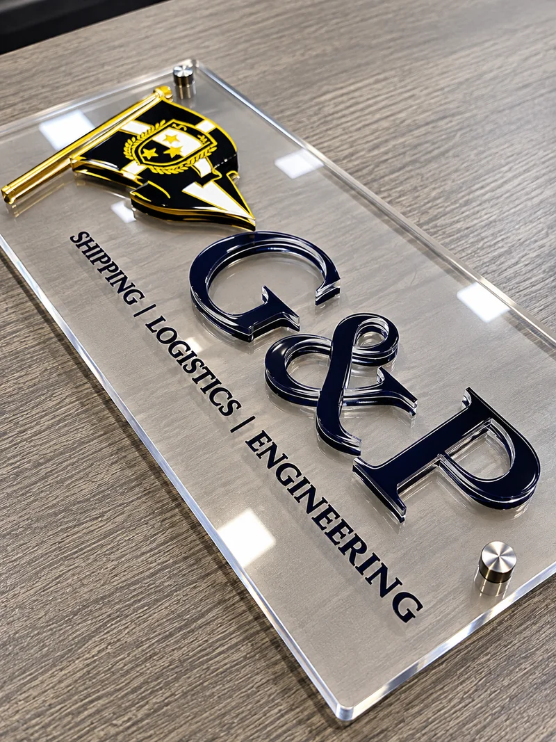 Aviso transparente con logotipo y letras oscuras elevadas sobre una base rectangular.